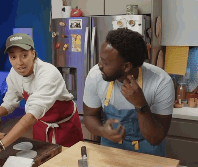 a man and a woman are cooking in a kitchen and the man is wearing a hat that says ' idea '