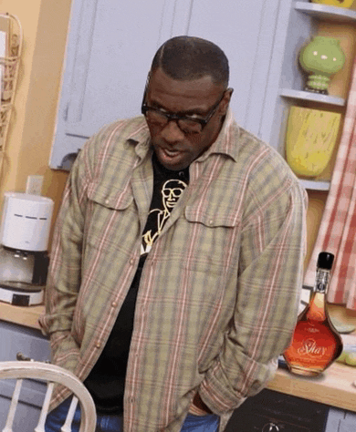 a man in a plaid shirt stands in a kitchen next to a bottle of shar