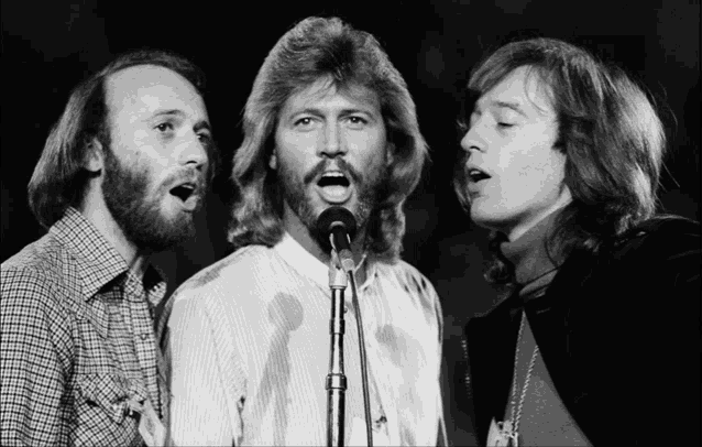 three men singing into microphones one of whom has a beard