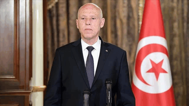 a man in a suit and tie is standing in front of a flag with a red star on it .