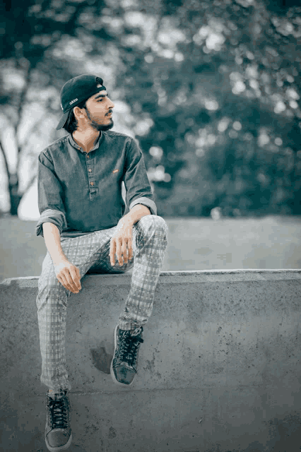 a man wearing a baseball cap sits on a concrete wall