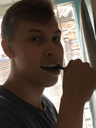 a young man brushing his teeth with a black brush