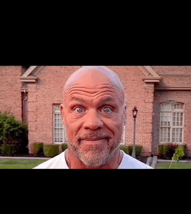 a bald man with a beard makes a funny face in front of a brick house