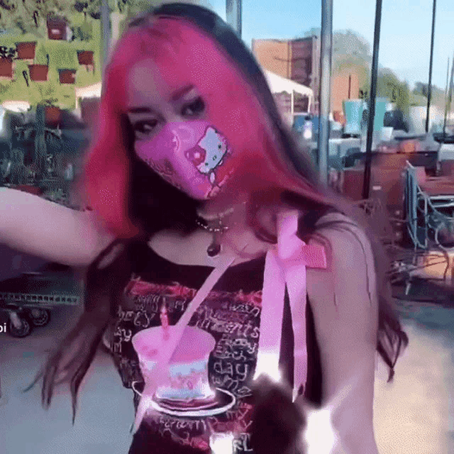 a girl with pink hair and a hello kitty mask is holding a pink cup .