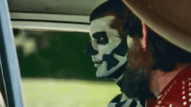 a man with a skeleton mask on his face is looking out of a car window .