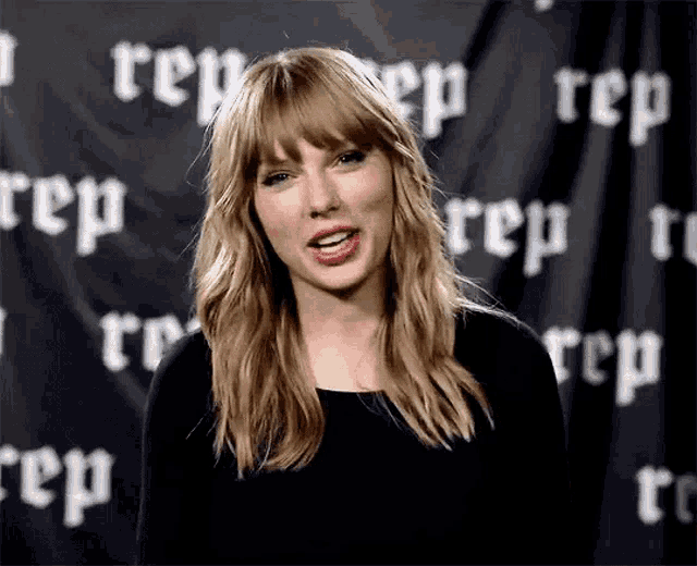 a woman with blonde hair and bangs is standing in front of a black curtain with the word rep on it .