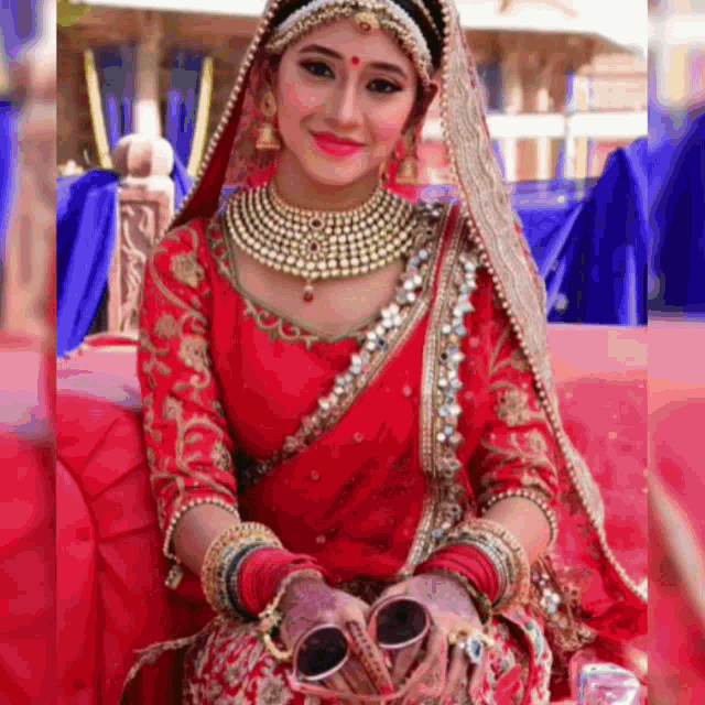 a bride in a red dress is sitting on a couch holding a pair of wedding rings in her hands .