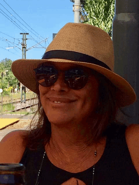 a woman wearing a straw hat and sunglasses smiles for the camera