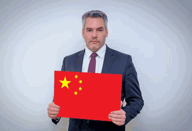 a man in a suit and tie is holding up a red flag with yellow stars