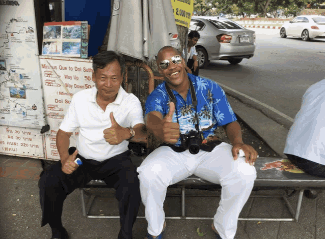 two men are giving a thumbs up in front of a sign that says " minibus que to doi sut "