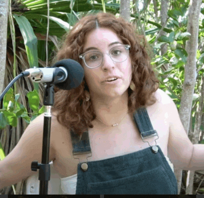 a woman wearing overalls and glasses is speaking into a microphone