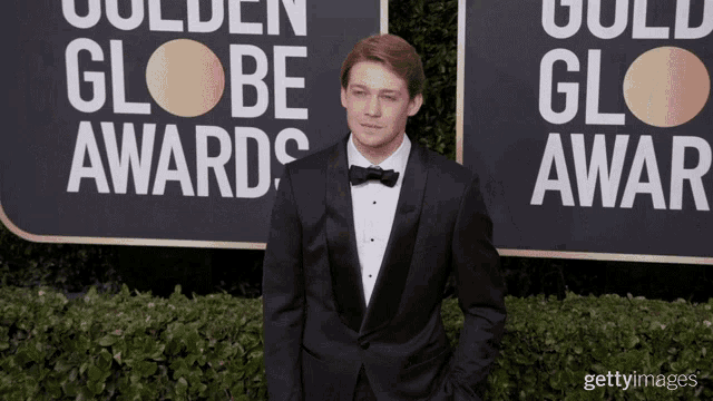 a man in a tuxedo stands on a red carpet in front of a sign that says golden globe awards