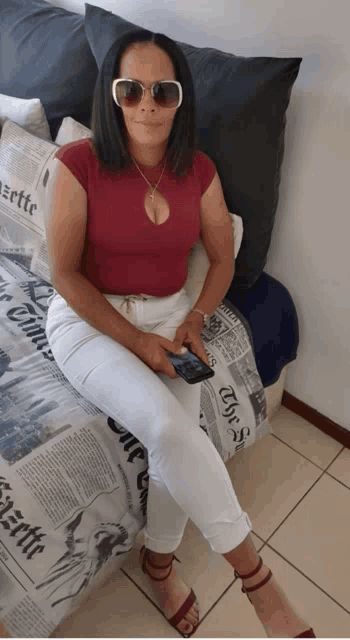 a woman wearing sunglasses sits on a bed with a newspaper cover