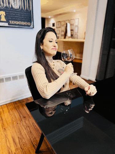 a woman sits at a table holding a glass of wine