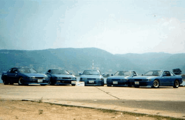 four blue cars are parked next to each other on a sunny day