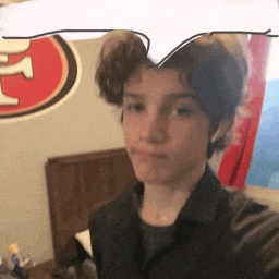 a young boy is taking a selfie in a bedroom with a san francisco 49ers logo on the wall behind him .