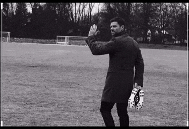 a man in a trench coat holds a pair of soccer cleats in his hand