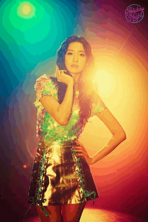 a woman in a sequined top and metallic skirt is standing in front of a colorful light .