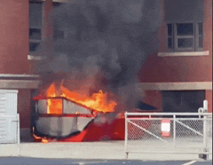 a dumpster is on fire in front of a brick building with smoke coming out of it