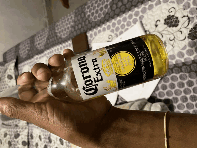 a hand holding a bottle of corona extra beer