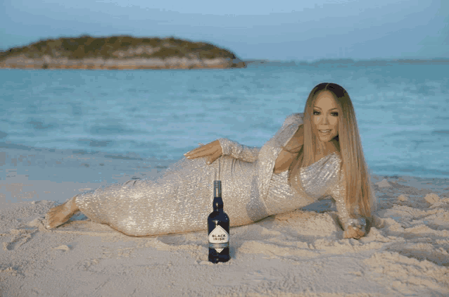 a woman in a sequined dress is laying on the beach next to a bottle of black label vodka