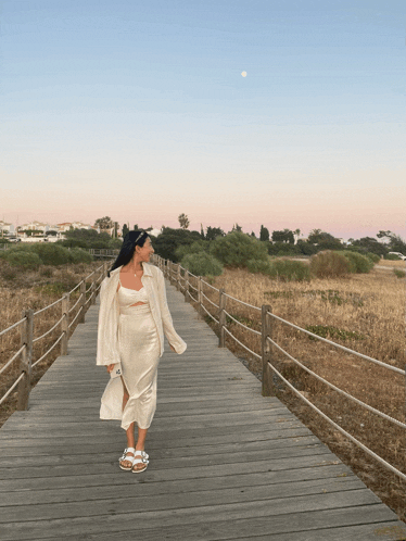 a woman in a white dress stands on a wooden bridge