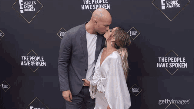 a man and woman kiss on a red carpet in front of a wall that says the people have spoken