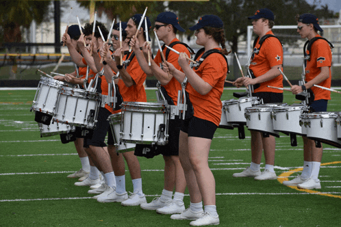 a marching band is playing their drums on a field and they are wearing orange shirts