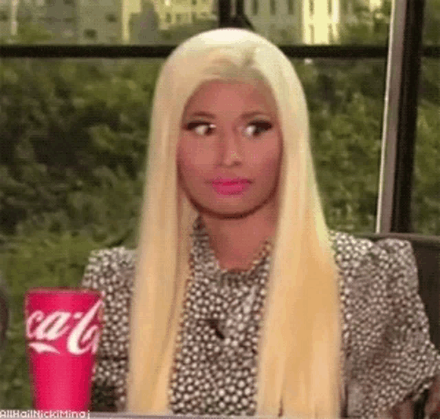 a woman with long blonde hair is sitting at a table with a coca cola cup in her hand .