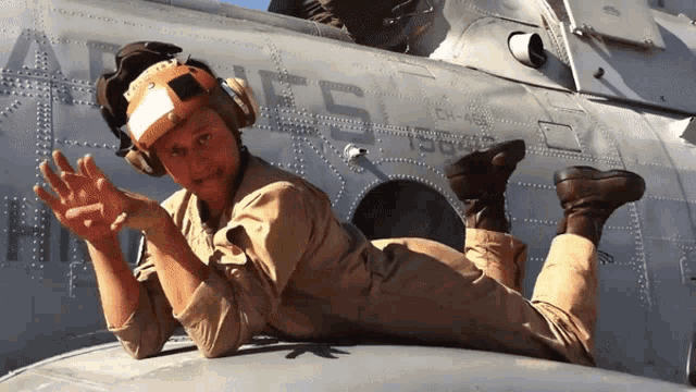 a man in a military uniform is laying on the wing of a plane with the letters a and h on it