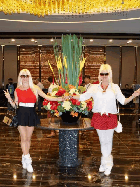 two women standing in front of a table with flowers in it