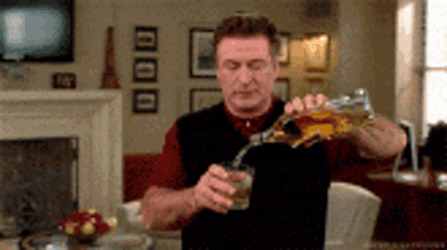 a man is pouring a drink into a glass in a living room .