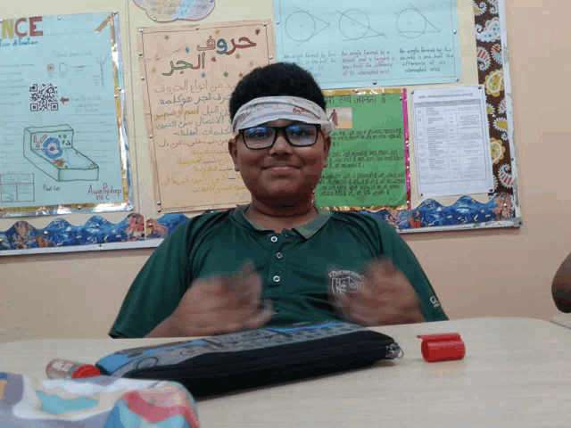 a boy wearing glasses and a bandana is sitting at a desk in front of a bulletin board that says " once "