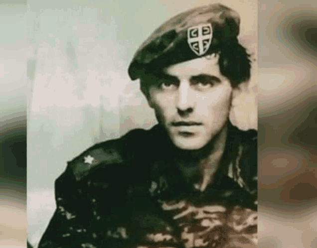 a man in a military uniform is wearing a beret with the letter gb on it .