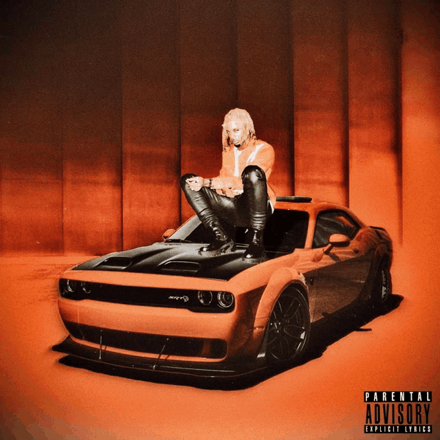 a man sits on the hood of an orange dodge challenger with parental advisory explicit lyrics