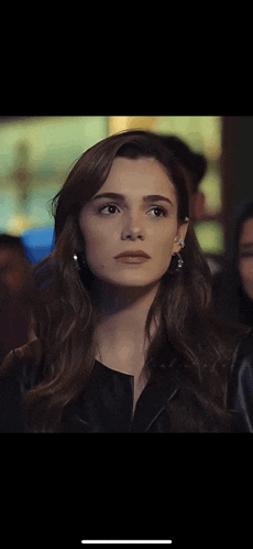 a close up of a woman wearing earrings and a leather jacket looking at the camera .