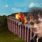 a young man with glasses is smiling in front of a bridge with a train on it