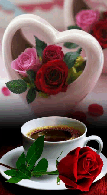 a cup of coffee with roses in a heart shaped vase behind it