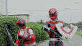 two red power rangers are standing next to each other on a street .