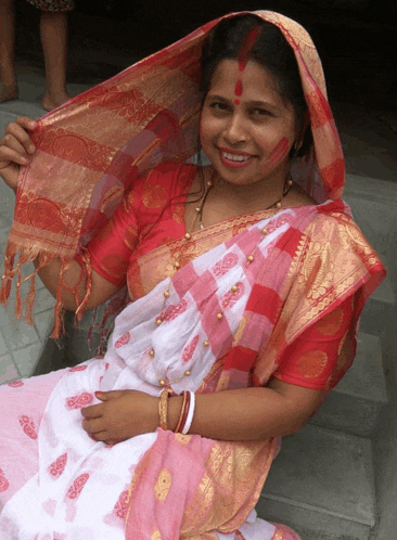 a woman wearing a pink and white dress and a red head scarf smiles