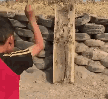 a young boy in a red shirt is standing in front of a pile of tires and a piece of wood .