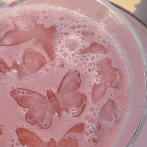 a close up of a pink milkshake with butterfly shaped ice cubes in it .