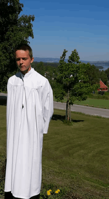 a young man in a white robe is standing in a grassy field