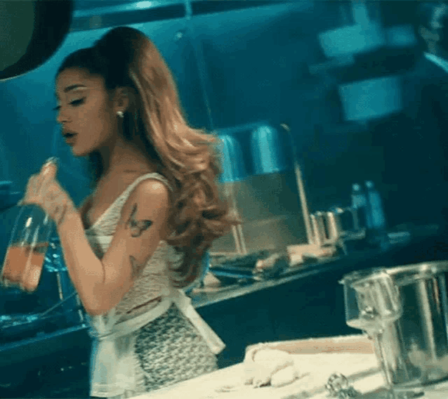 ariana grande is standing in a kitchen drinking from a bottle .