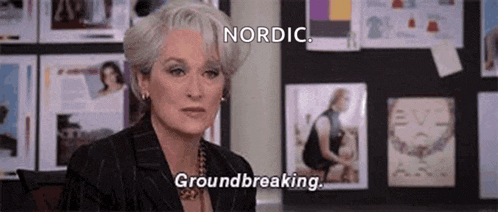 a woman with gray hair is sitting in front of a wall with pictures on it and says `` nordic , groundbreaking . ''