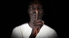 a man in a white shirt is making a silence gesture with his finger to his lips .