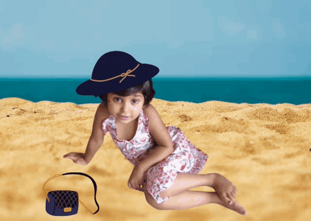 a little girl wearing a hat and a dress is laying on the beach