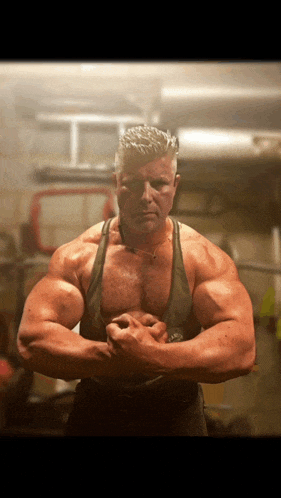 a man with a necklace around his neck is flexing his muscles in a gym