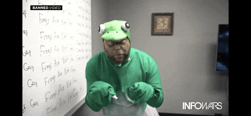 a man in a green frog costume is writing on a whiteboard