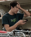 a man in a black shirt is sitting in a shopping cart looking at his phone .